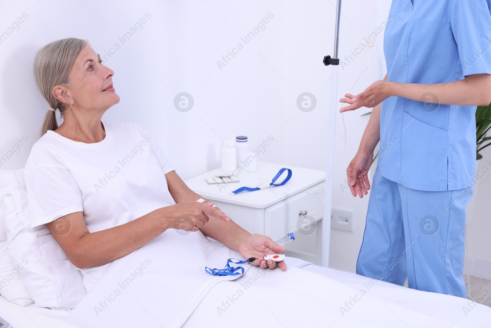 Photo of Nurse and senior woman talking about emergency call button in hospital, closeup