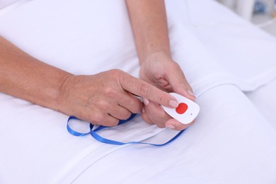 Photo of Senior woman pressing emergency call button on bed in hospital, closeup