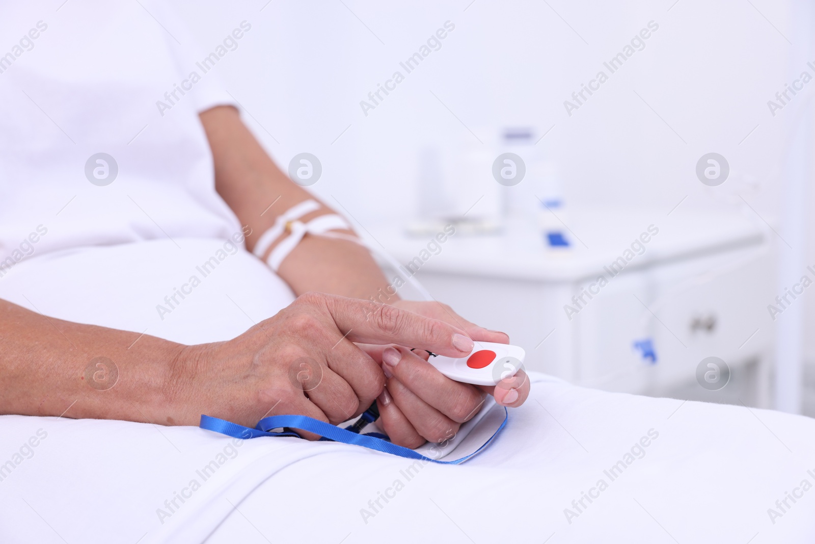 Photo of Senior woman pressing emergency call button on bed in hospital, closeup