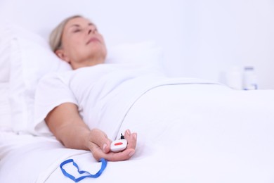 Senior woman with emergency call button on bed in hospital, selective focus