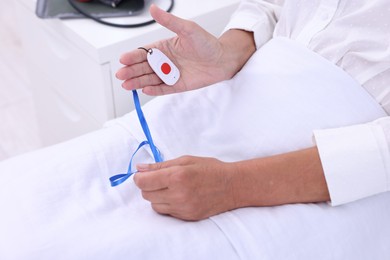 Photo of Senior woman with emergency call button on bed in hospital, closeup