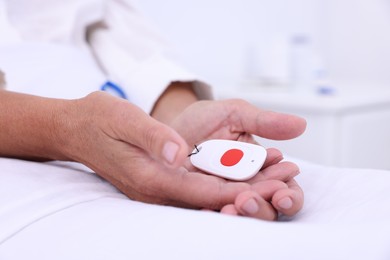 Photo of Senior woman with emergency call button on bed, closeup