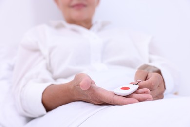 Senior woman with emergency call button on bed in hospital, closeup