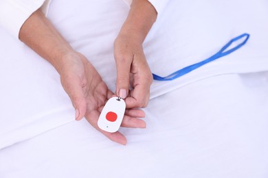 Photo of Senior woman with emergency call button on bed in hospital, top view