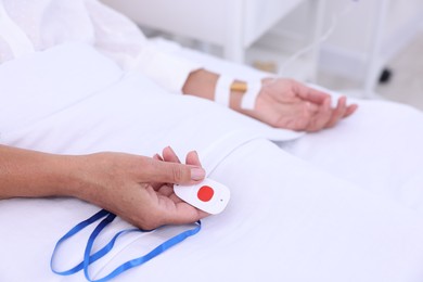 Senior woman with emergency call button on bed in hospital, closeup