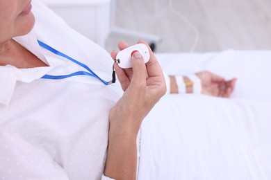 Senior woman pressing emergency call button on bed in hospital, closeup