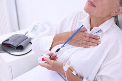 Senior woman suffering from heart pain pressing emergency call button on bed in hospital, closeup