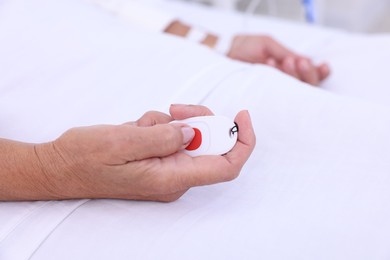 Photo of Senior woman pressing emergency call button on bed in hospital, closeup