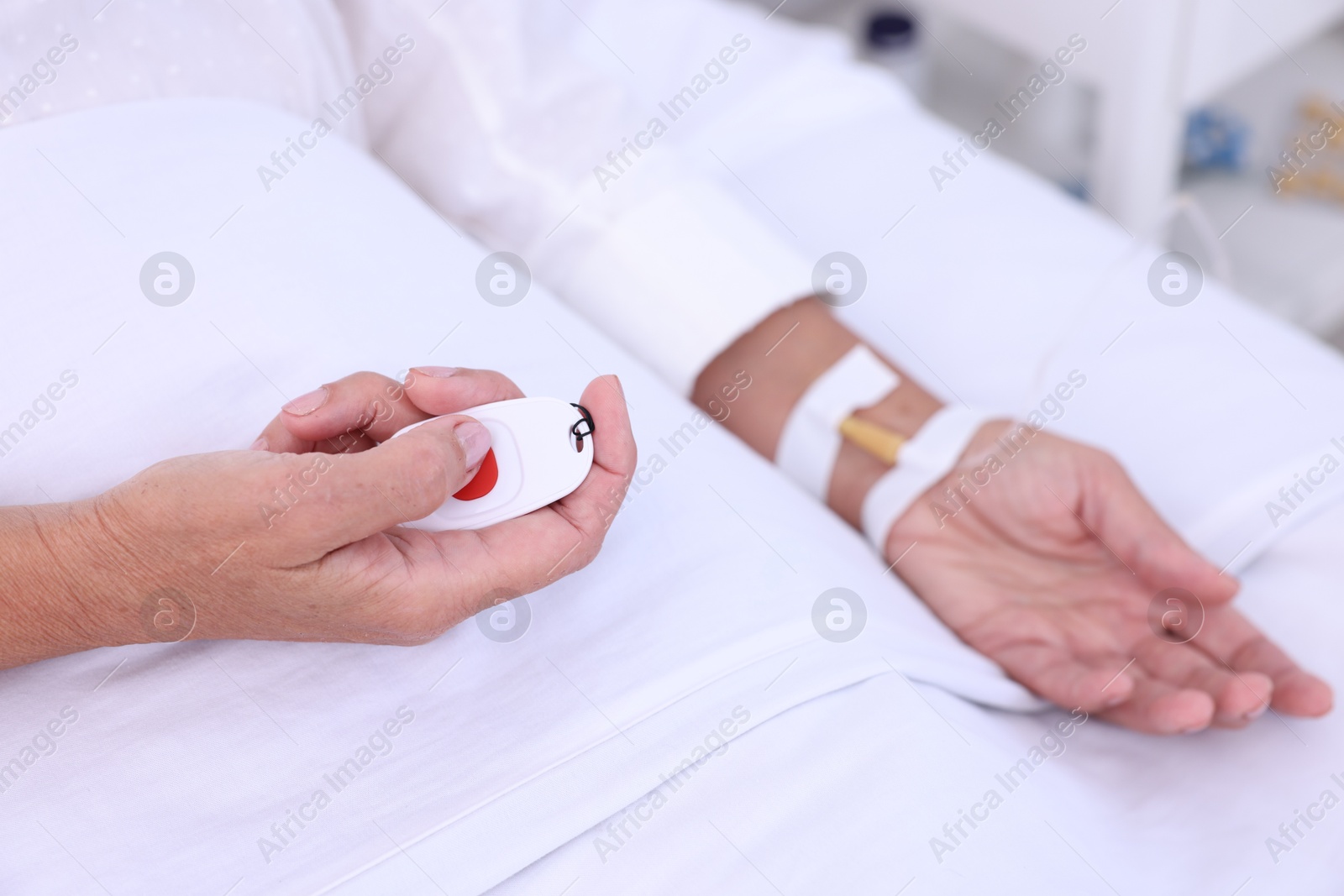 Photo of Senior woman pressing emergency call button on bed in hospital, closeup