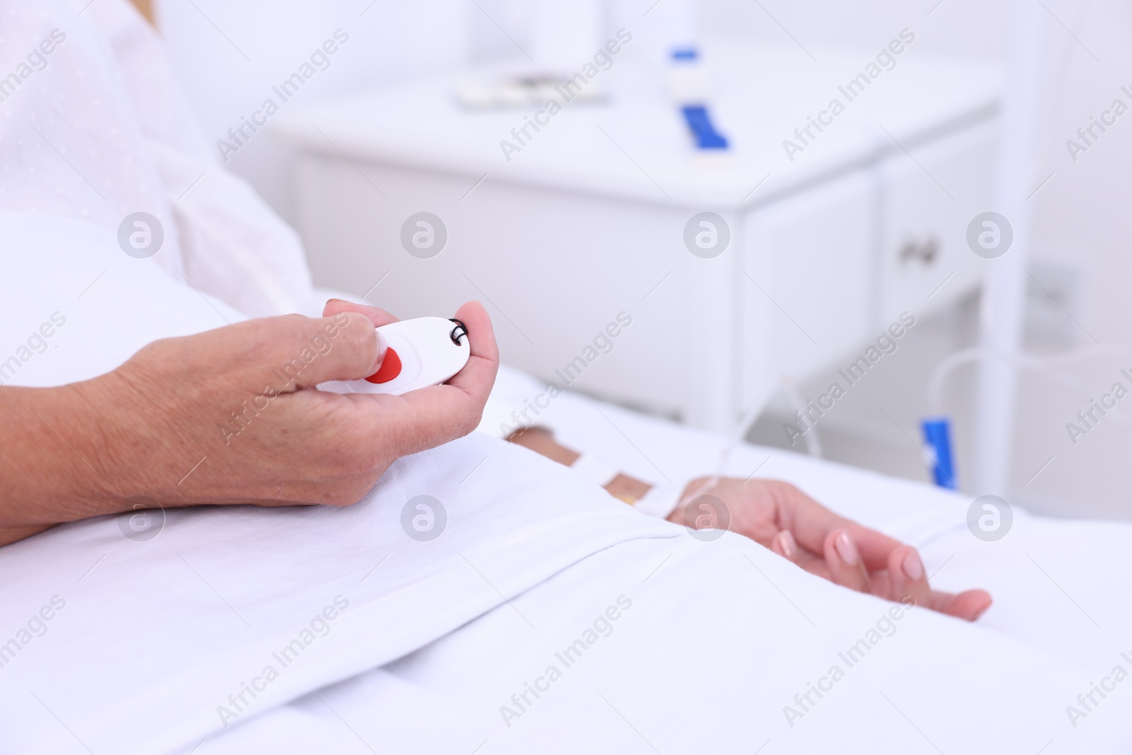 Photo of Senior woman pressing emergency call button on bed in hospital, closeup