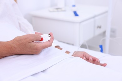 Photo of Senior woman pressing emergency call button on bed in hospital, closeup