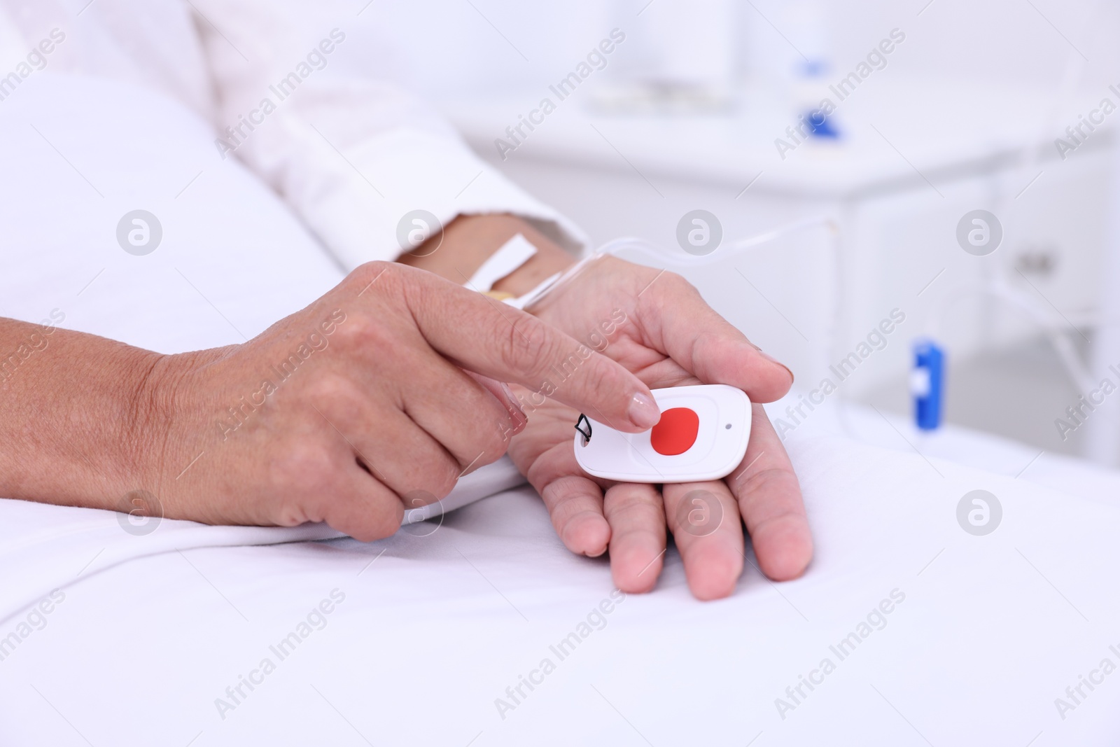 Photo of Senior woman pressing emergency call button on bed in hospital, closeup