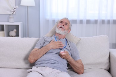 Photo of Senior man suffering from heart pain pressing emergency call button at home