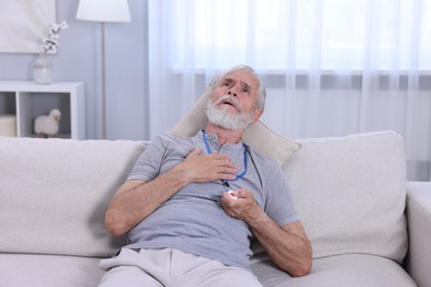 Senior man suffering from heart pain pressing emergency call button at home