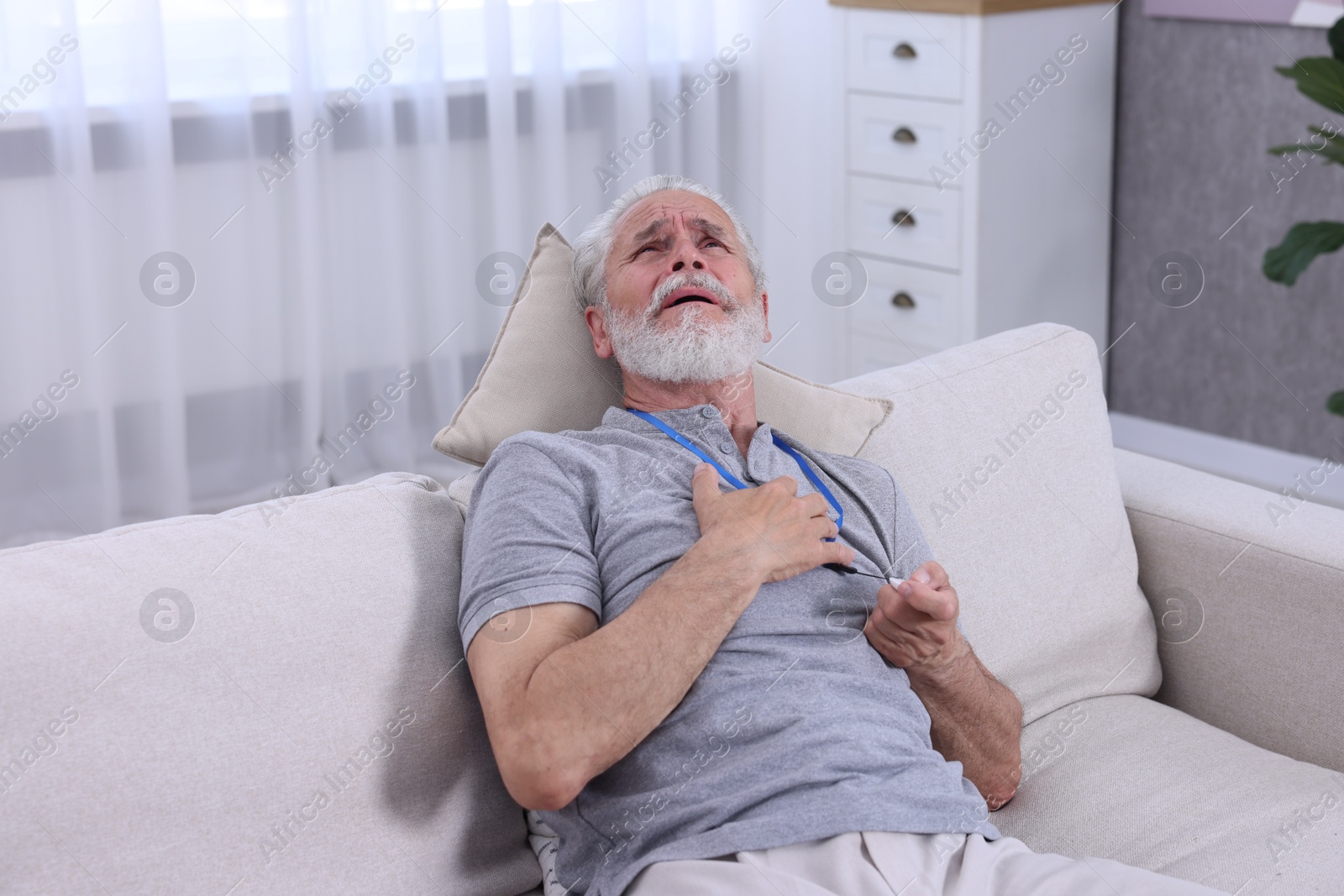 Photo of Senior man suffering from heart pain pressing emergency call button at home