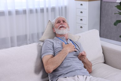 Photo of Senior man suffering from heart pain pressing emergency call button at home