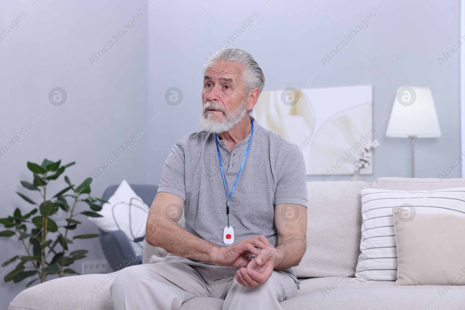 Photo of Senior man with emergency call button checking pulse on wrist at home