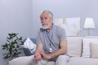 Photo of Senior man with emergency call button checking pulse on wrist at home