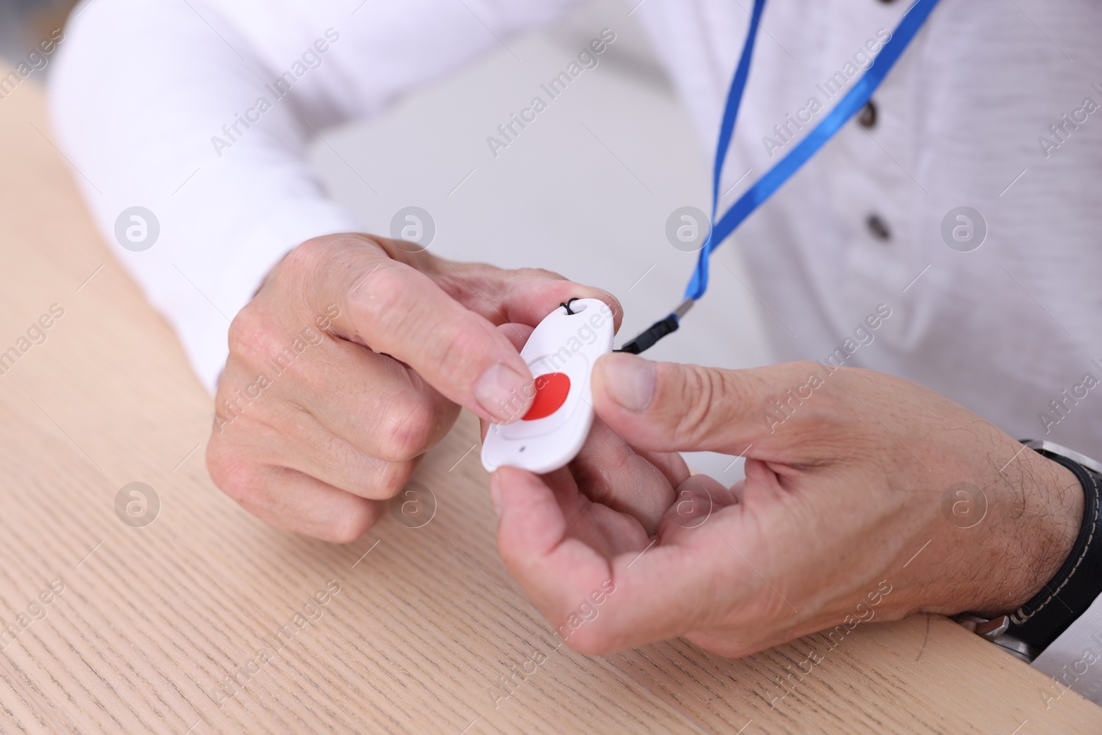 Photo of Senior man with emergency call button at wooden table, closeup