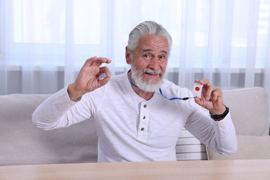 Photo of Happy senior man with emergency call button showing OK gesture at home