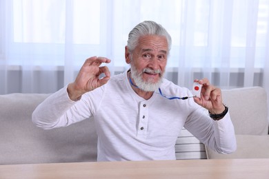 Happy senior man with emergency call button showing OK gesture at home