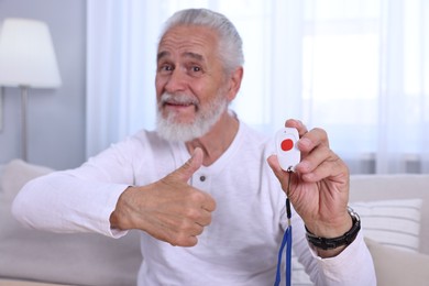 Photo of Happy senior man with emergency call button showing thumbs up at home, selective focus