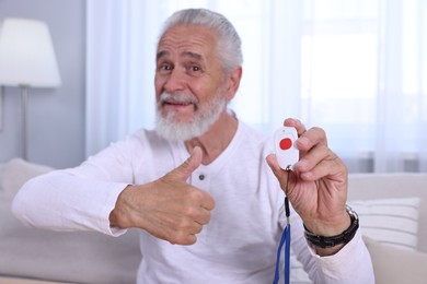 Happy senior man with emergency call button showing thumbs up at home, selective focus