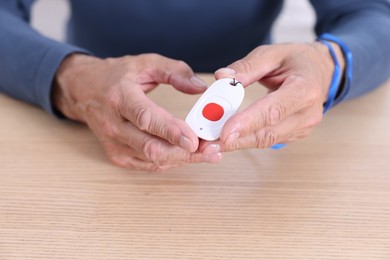 Photo of Senior man with emergency call button at wooden table, closeup