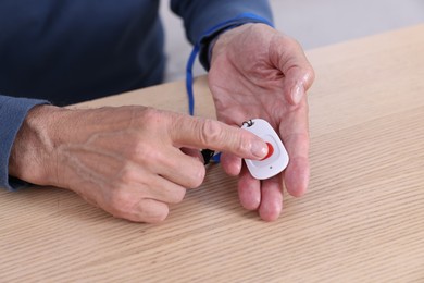 Photo of Senior man with emergency call button at wooden table, closeup