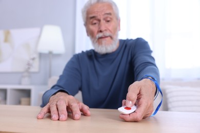 Photo of Senior man pressing emergency call button at home, selective focus