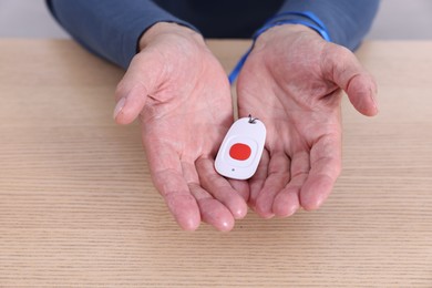 Photo of Senior man with emergency call button at wooden table, closeup