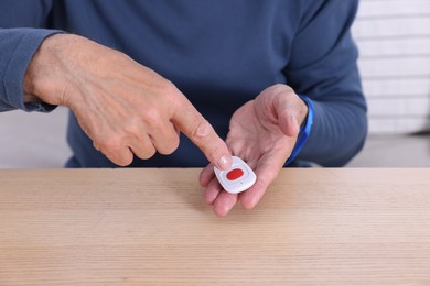 Photo of Senior man with emergency call button at wooden table, closeup