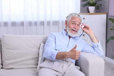 Photo of Happy senior man with emergency call button showing thumbs up at home