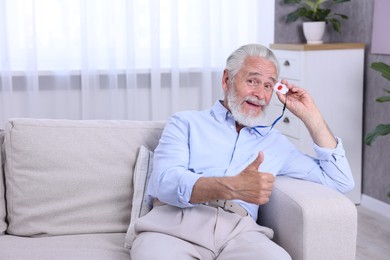 Happy senior man with emergency call button showing thumbs up at home