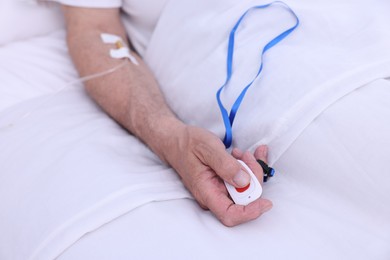 Senior man pressing emergency call button on bed in hospital, closeup