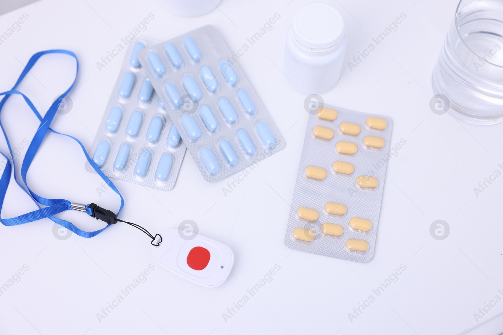 Photo of Emergency call button, pills and glass of water on white table, above view