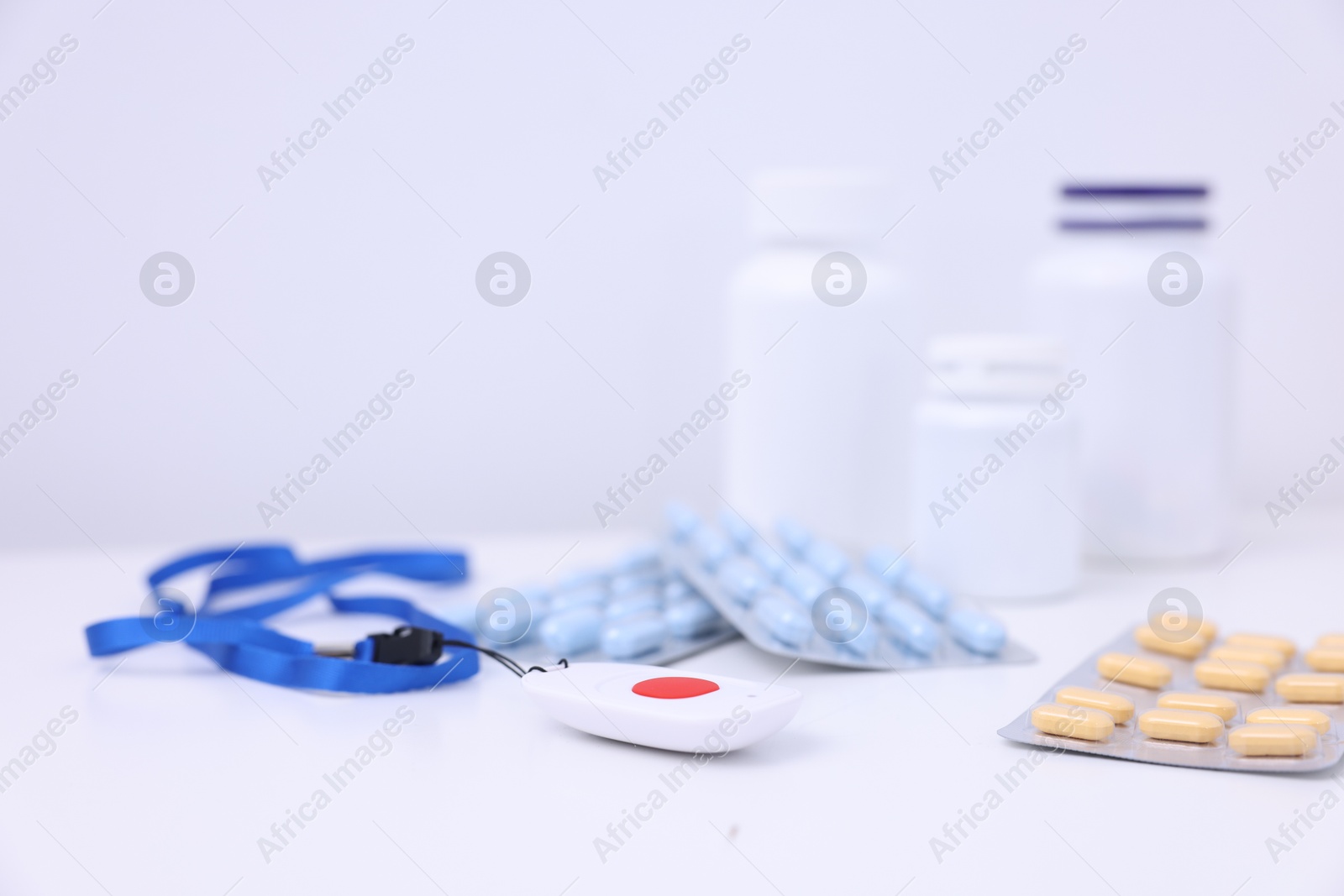 Photo of Emergency call button and pills on white table