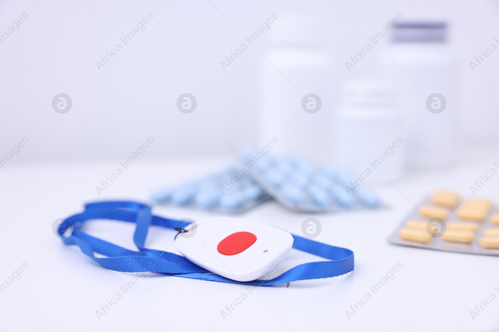 Photo of Emergency call button and pills on white table, closeup