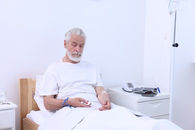 Senior man pressing emergency call button on bed in hospital