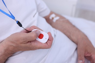 Senior man pressing emergency call button on bed in hospital, closeup