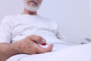 Senior man with emergency call button on bed in hospital, closeup