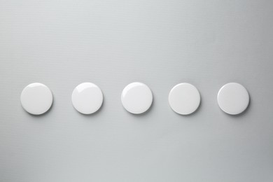 Blank white button badges on grey background, top view. Mockup for design