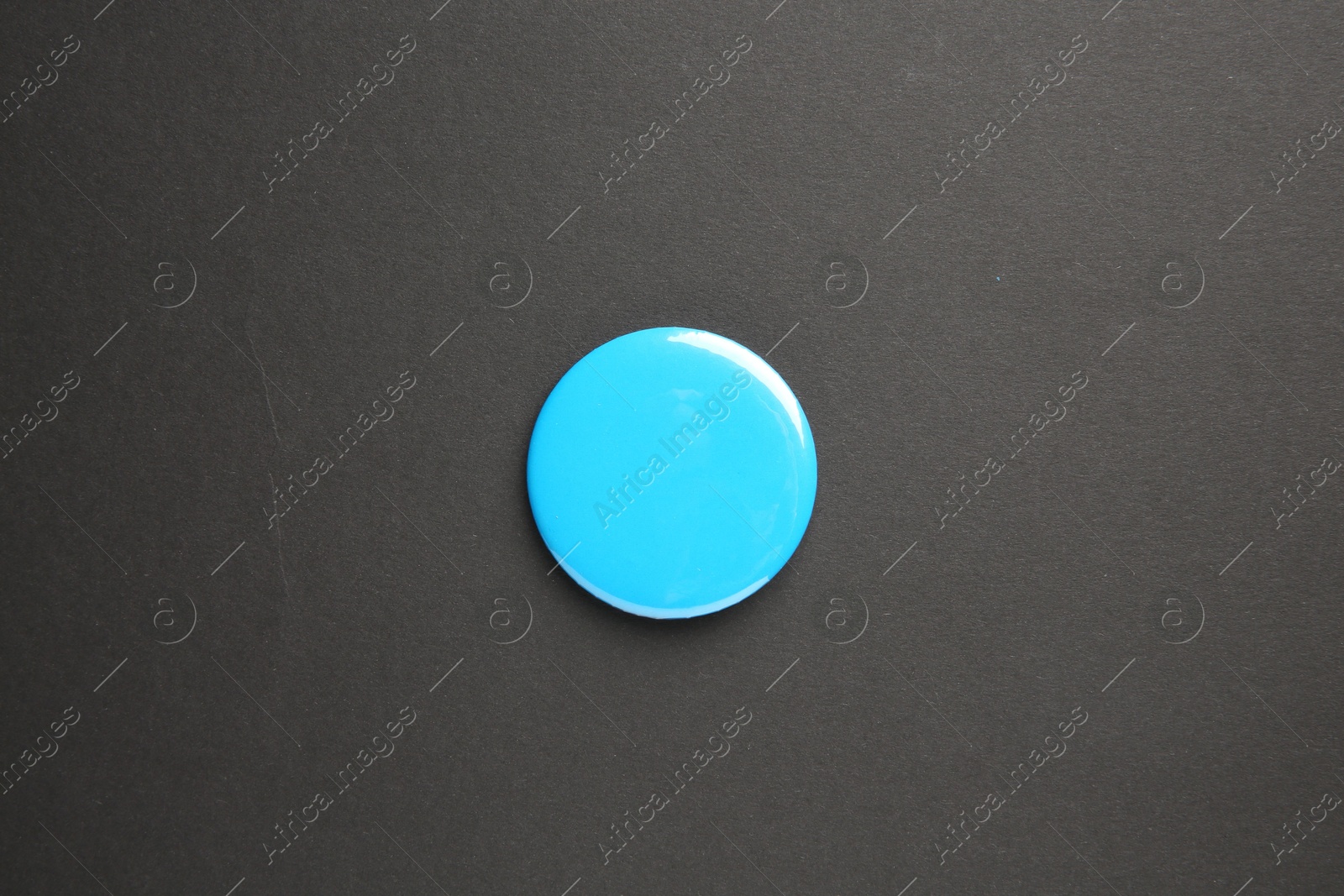 Photo of Blank light blue button badge on black background, top view. Mockup for design