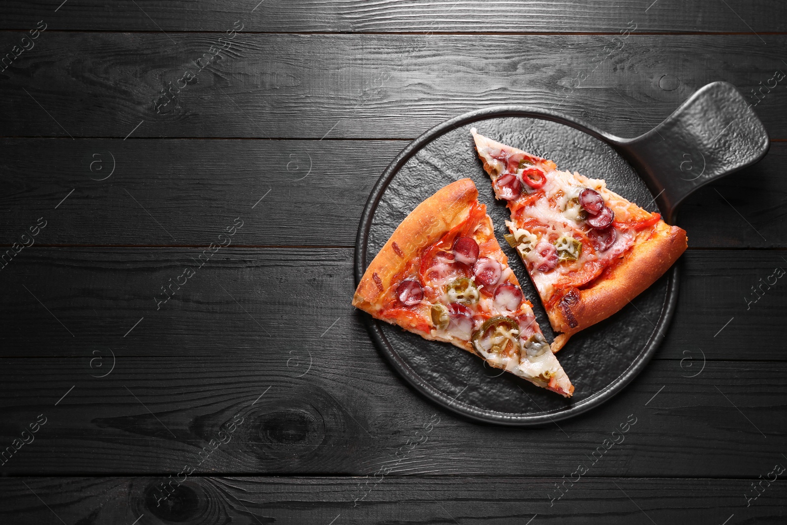 Photo of Board with pieces of delicious pizza Diablo on black wooden table, top view. Space for text