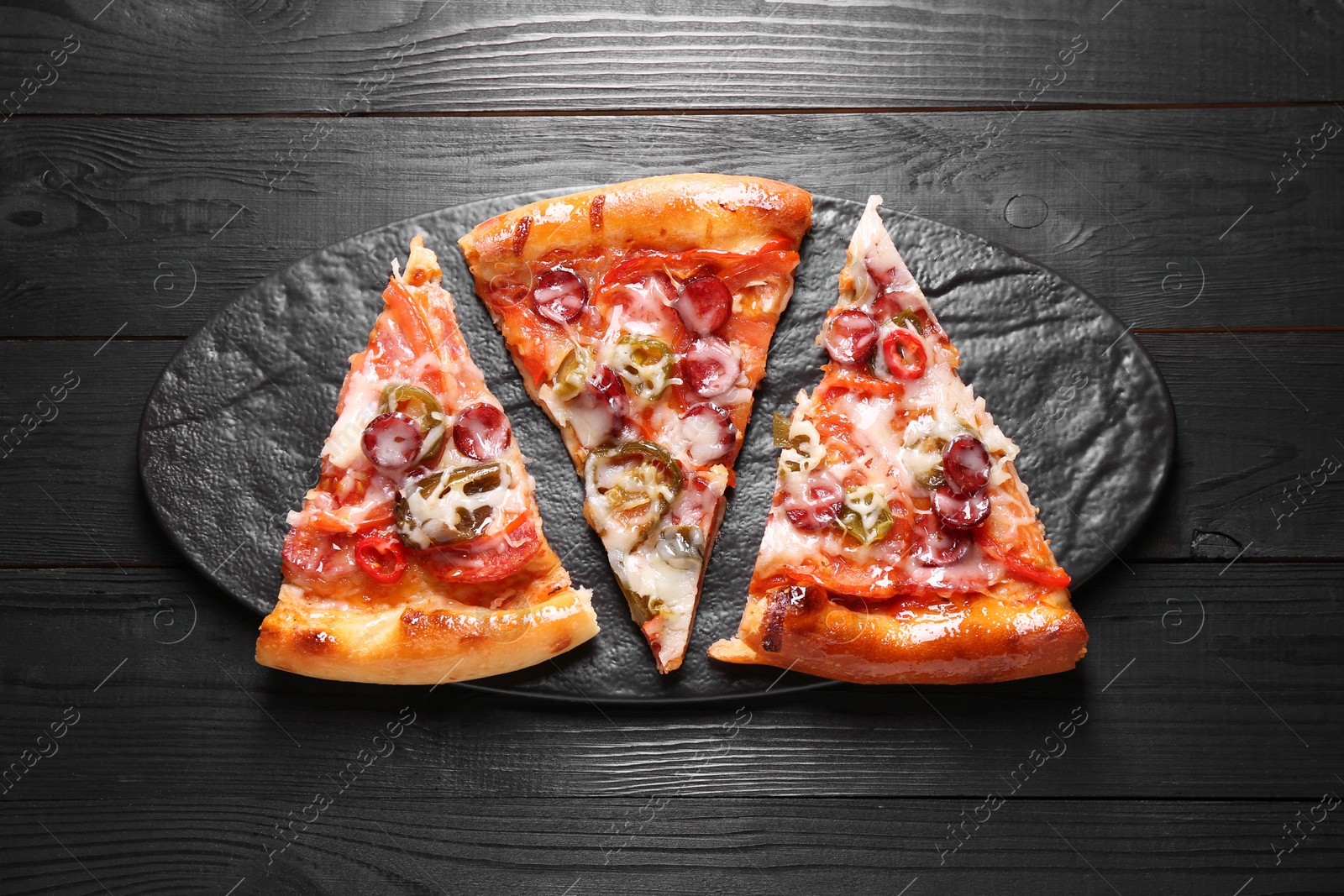 Photo of Slate board with pieces of delicious pizza Diablo on black wooden table, top view