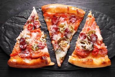 Photo of Slate board with pieces of delicious pizza Diablo on black wooden table, top view