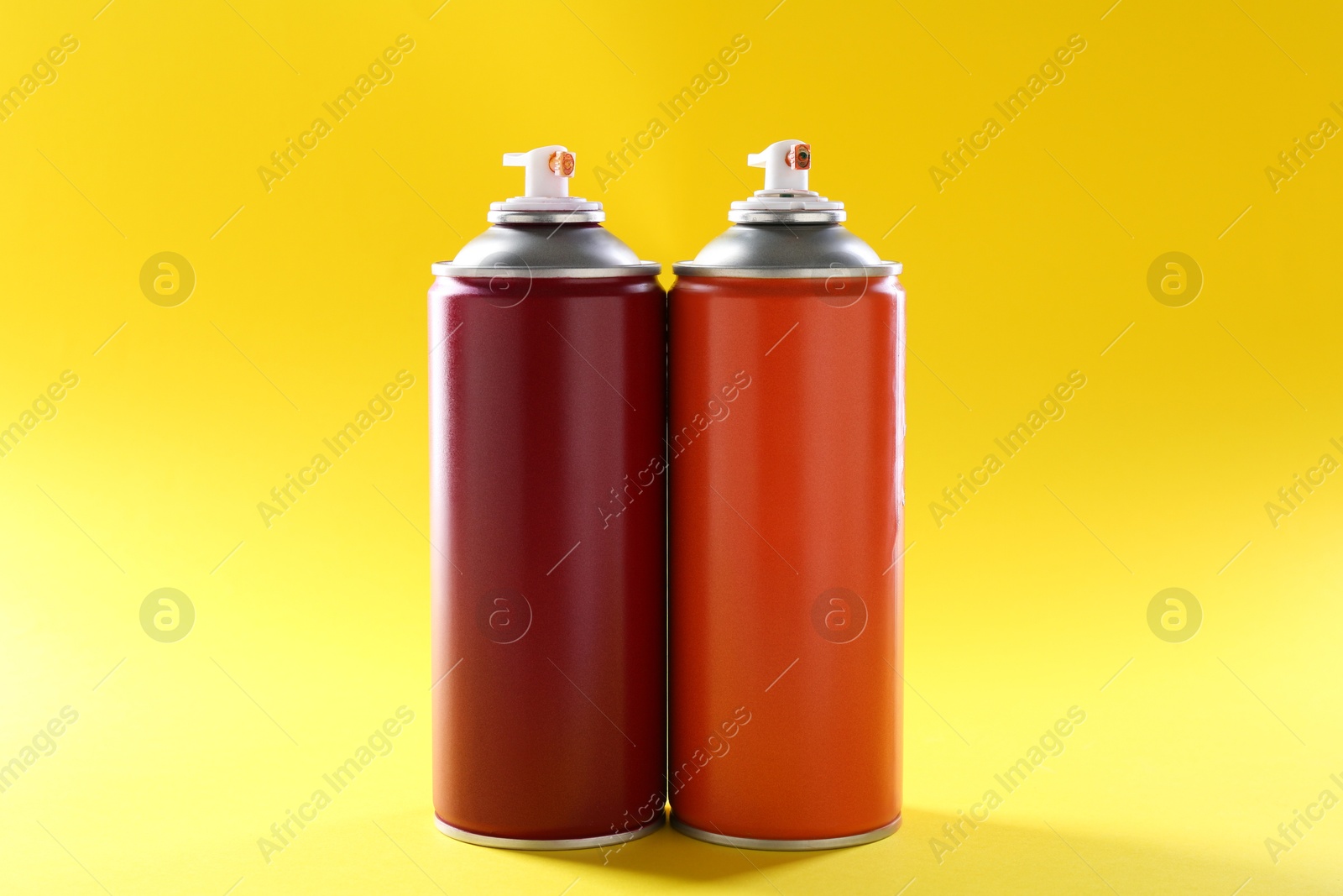 Photo of Two spray paint cans on yellow background