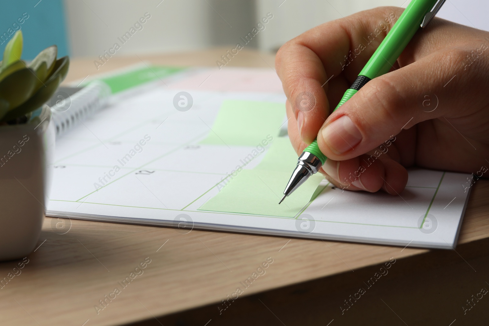 Photo of Timetable. Man making schedule using calendar and sticky note at wooden table, closeup