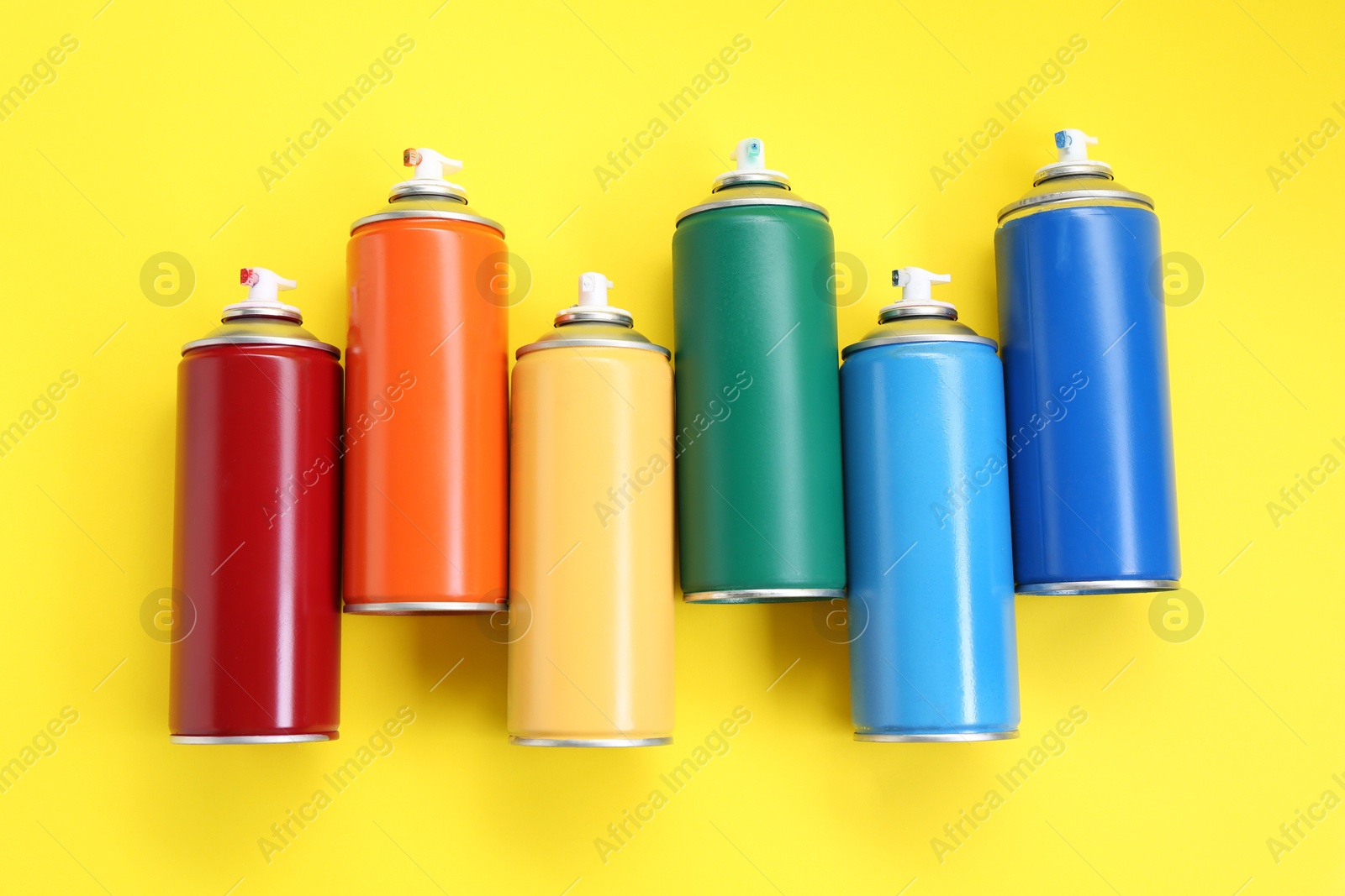 Photo of Many spray paint cans on yellow background, top view