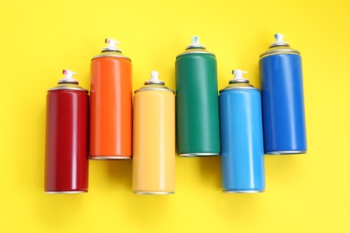 Photo of Many spray paint cans on yellow background, top view